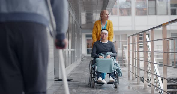 Female Nurse Pushing a Disabled Man in Wheelchair Outside Hospital