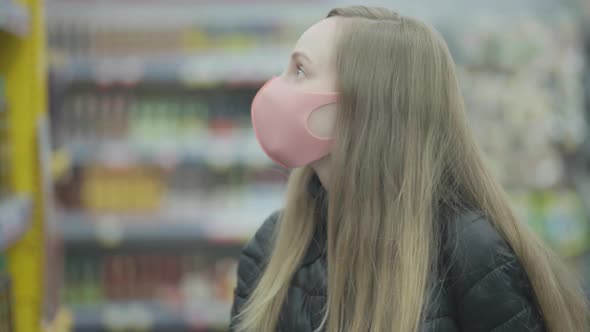 Covid-19 Coronovirus, Pandemic. Serious Young Blonde Girl Stands in Mask Gloves with Cart in