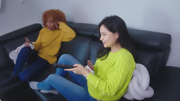 Best Friends Asian and African American Black Women Watching Tv and Eating Chocolate. 