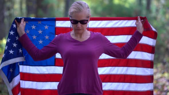 Blonde woman raising an American flag behind her with serious expression.