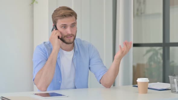 Angry Young Creative Man Talking on Smartphone in Office