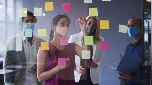 Diverse business colleagues wearing face masks standing brainstorming in office