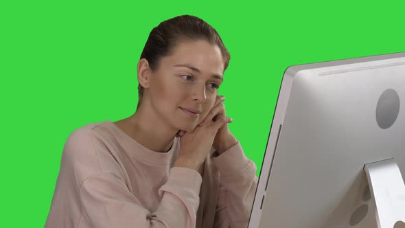 Blonde Girl with Pink Pullover Looking at Monitor of Computer Watching Video on a Green Screen