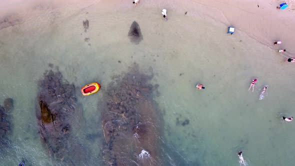 Aerial top down shot of people relaxing at the beach and an empty inflatable boat on the water. Jib
