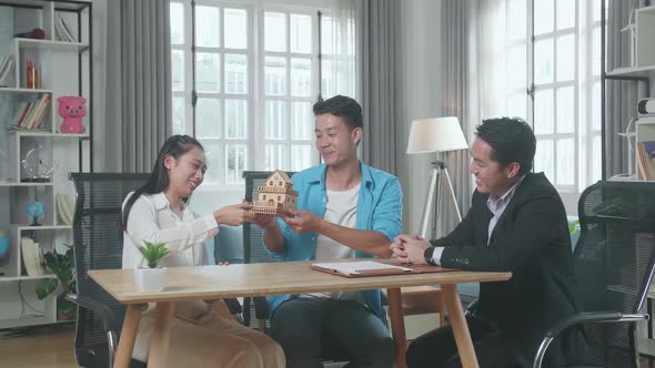 Asian Real Estate Agent With A House Purchase Contract Paper Giving A House Model To A Couple