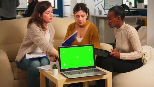 Diverse Women Sitting at Table Discussing Strategy with Green Screen Laptop