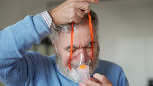 Closeup of Senior Bearded Man Putting on Nebulizer Indoors