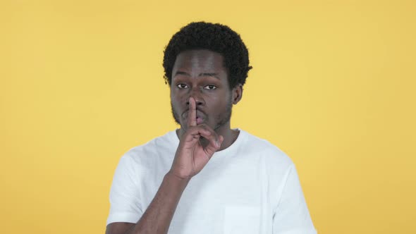 African Man Gesturing Silence, Finger on Lips, Yellow Background