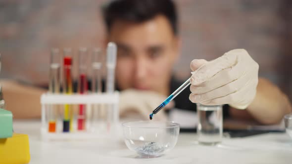 Chemist with Gloves Drops Blue Reagent in Bowl with Crystals