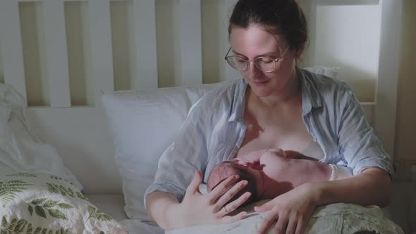 An adult woman in a home bedroom is breastfeeding a newborn baby