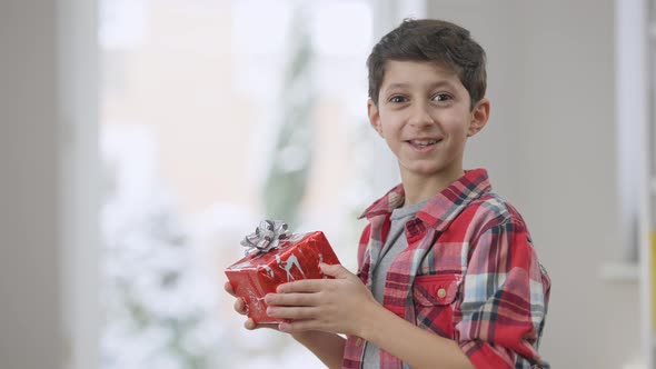 Portrait of Excited Cute Middle Eastern Boy Shaking Gift and Looking at Camera Smiling with