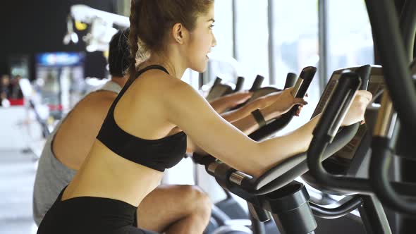 Attractive Asian Woman Riding on the Spinning Bike at the Gym and Looking at Camera