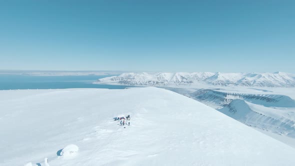 Team of hikers reaching snowy mountain top in majestic landscape of Svalbard