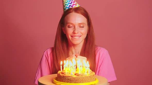 Redhaired Ginger Woman in Pink Studio Background Making a Wishes