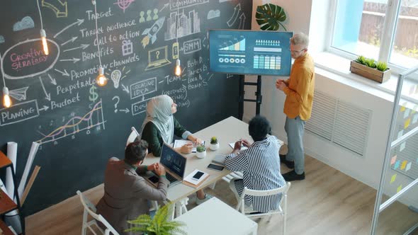 High Angle View of Young Employee Making Presentation to Group of Colleagues in Office