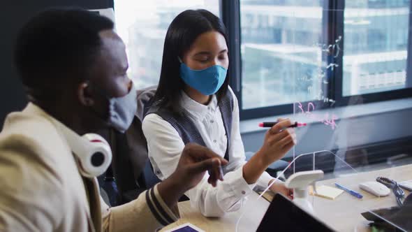 African american man and asian woman writing on glass board at modern office