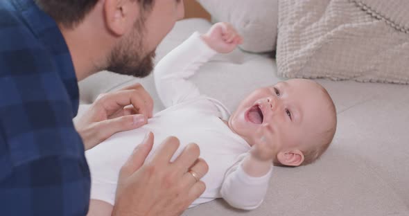 Close Up of the Baby Lying on Its Back on the Couch Smiling and Happy Looking at Its Father Who is