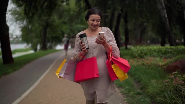 Front View Portrait Confident Satisfied Woman with Shopping Bags Walking in Park Surfing Social