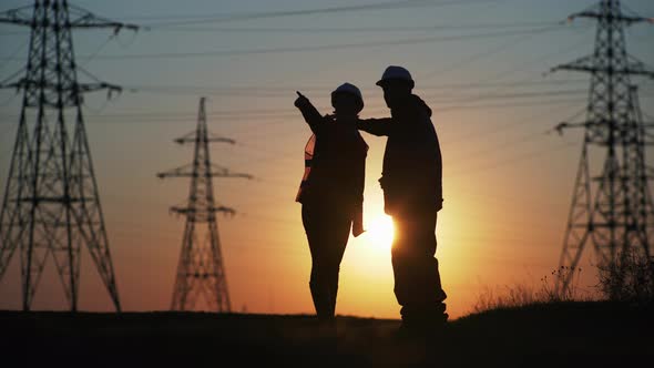 Silhouette, Male and Female Engineers in Protective Helmets Gesturing with Their Hands, Discussing