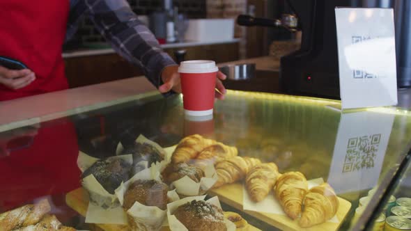 Mixed race male barista receiving contactless smartphone payment for takeaway coffee