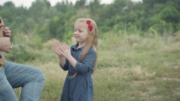 Cheerful Little Girl Clapping Supporting Unrecognizable Man Playing Ukulele