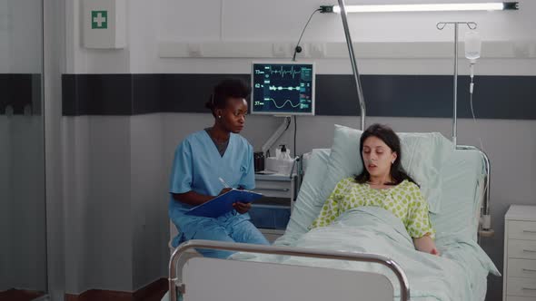 Sick Woman Resting in Bed While Afroamerican Nurse Monitoring Disease