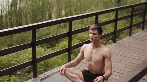 A calm half-naked guy with closed-eyes is doing meditation on the bridge