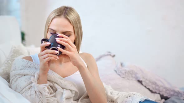 Adorable Smiling Girl Holding Mug Sitting on Couch Wrapped in Plaid and Relaxing