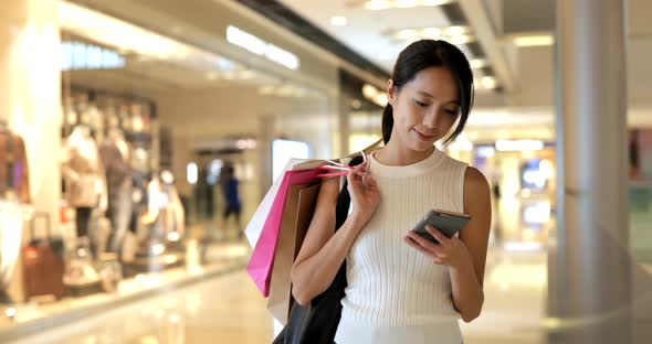 Woman using smart phone with shopping bags 