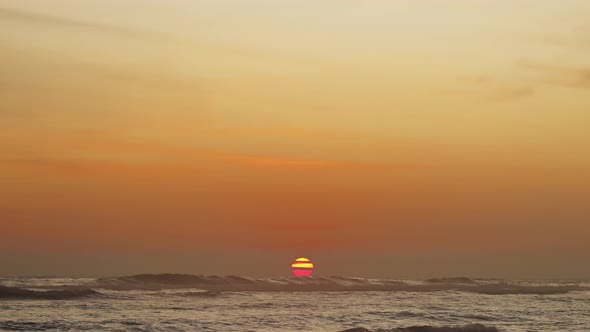 Sunset Timelapse with a Large Round Red Sun Hiding Behind the Horizon Line of Sea Waves