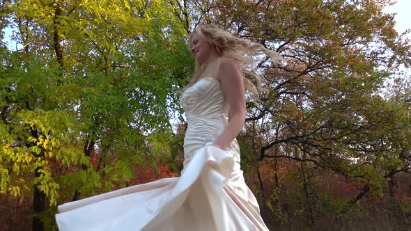 Blonde Woman in Wedding Dress Is Spinning at Autumn Colorful Forest.
