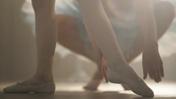Legs of Little Ballerina in Pointes in Backlit Fog As Unrecognizable Teacher Adjusting Tendu