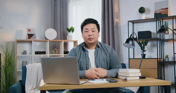 Asian Man Sitting in Front of Camera at His Workplace in Home Office