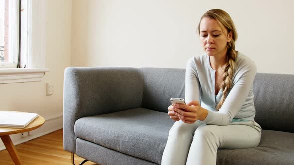 Woman using mobile phone on sofa in living room