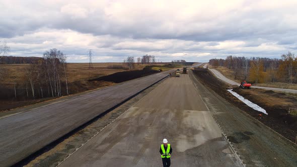 Worker in a Helmet is on the Construction of the Road