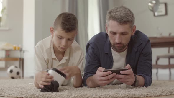 Dad and Son Laying on the Floor on the Fluffy Carpet Using Virtual Reality Glasses, Happy Friendly