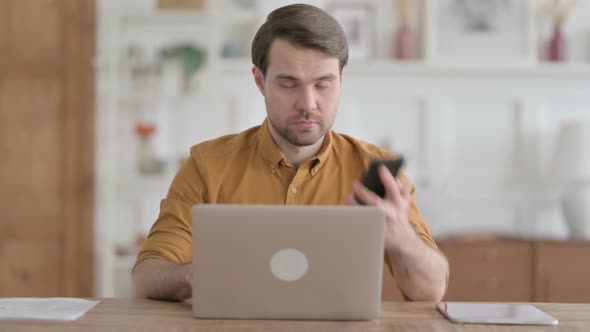 Young Man Talking on Phone while using Laptop in Office