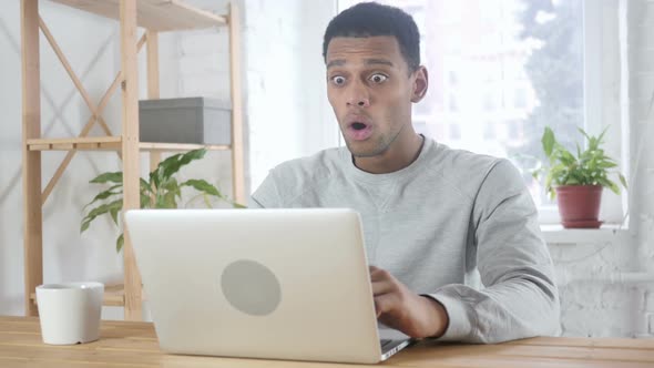 Shocked Wondering AfroAmerican Man Working on Laptop Sitting at Office