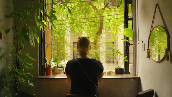 Walking Towards a Woman Looking out of a Window onto a Green Landscape