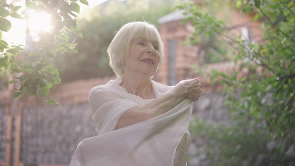 Beautiful Senior Woman in Wedding Dress Wrapping in White Shawl in Slow Motion Standing in Sunrays