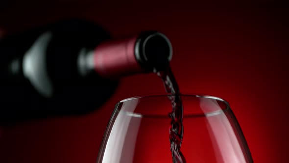 Super Slow Motion Detail Shot of Pouring Red Wine From Bottle on Luxury Red Background at 1000Fps