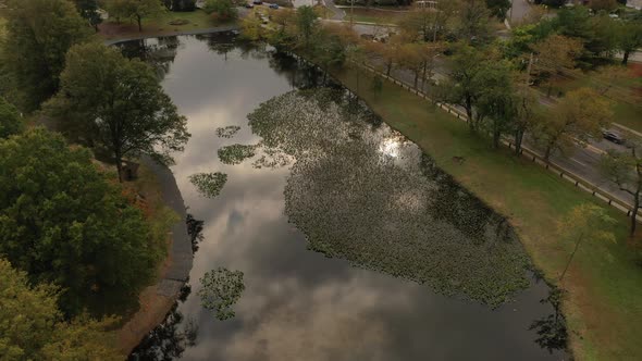 A drone shot of a pond on a cloudy day. The camera dolly in over the pond as the sun shines through