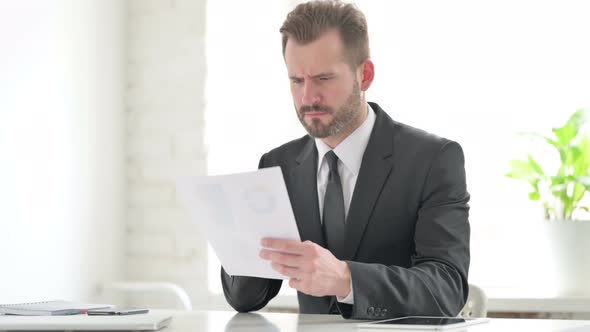 Young Businessman Upset While Reading Documents in Office