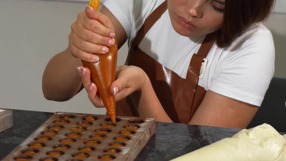Young Female Chocolatier Adding Filling Into Chocolate Molds