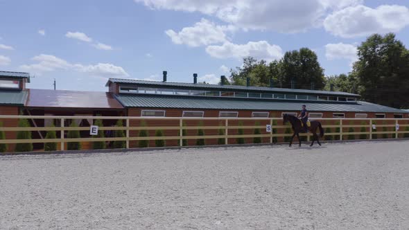 Young Caucasian Woman Rides on Horseback in Open Arena for Horses on the Hot Summer Day in the