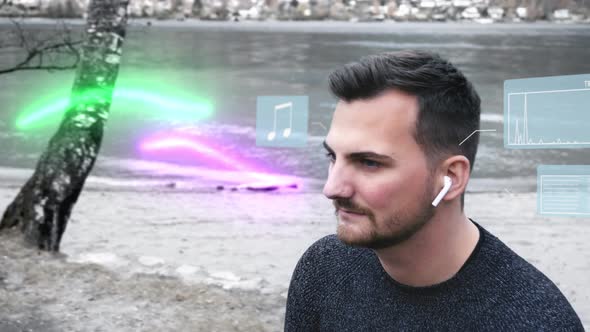 Man sitting on the shore of a mountain lake is diving into a world of his own while listening to mus