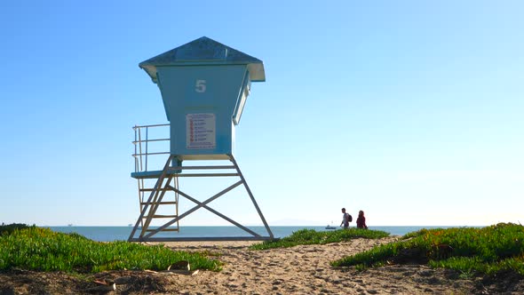 A lifeguard tower stands on the beach as a couple walks by in the background on the sandy beaches of