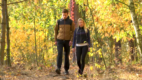 A Hiking Couple Walks Down a Path Through a Forest on a Sunny Day - Front View