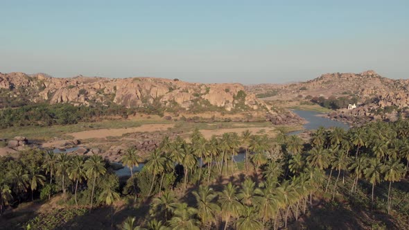 Paradisiac Tungabhadra Riverbank among rocky landscape and lush palm trees in Hampi, India