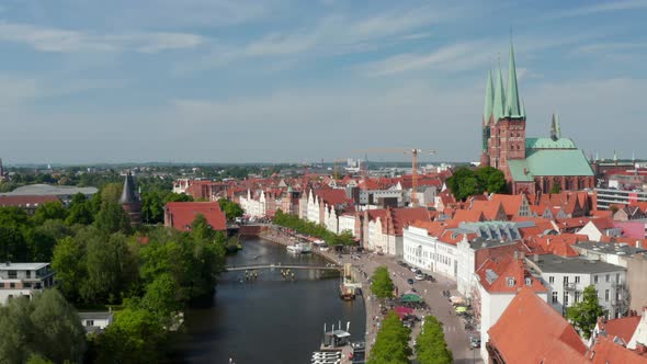 Forwards Descending Footage of Trave Waterfront with Moored Boats Restaurant Terraces and People